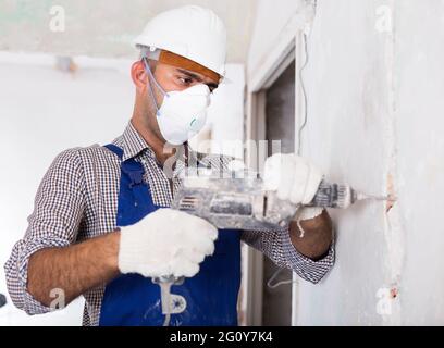 Adult male worker repairing with drill in mask Stock Photo