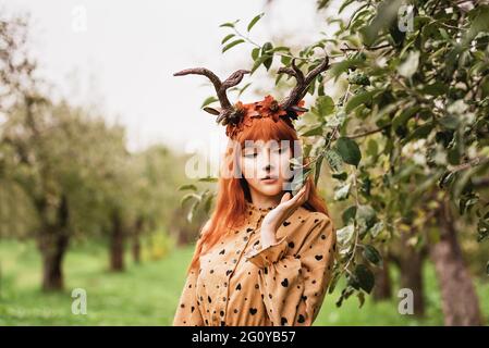 fairy woman with deer horns in autumn forest. Face painting. Beautiful mystery woman. redhead girl with big eyes magical sight Stock Photo