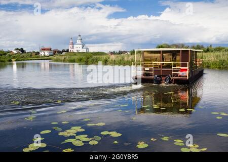 Suzdal, Russia, - June 25, 2016: Tourist boat going down the river with white church on the background Stock Photo