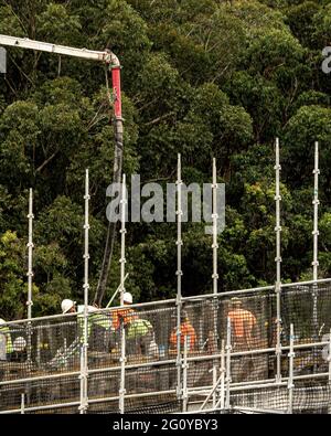 Workers close up spreading concrete delivered by Boom Pump on new building site with bushland backdrop. New social housing  at 56-58 Beane St. Gosford Stock Photo