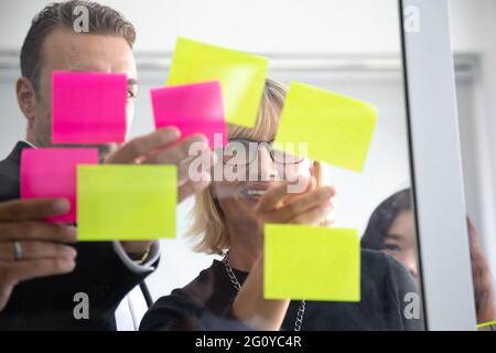 IT worker tracking his tasks on kanban board. Using task control of agile development methodology. Team members attaching sticky note to scrum task bo Stock Photo