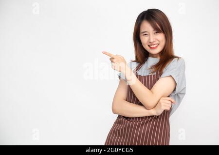 Portrait of Asian woman workers fresh market with brown apron standing and pointing finger to something isolated on white background Stock Photo
