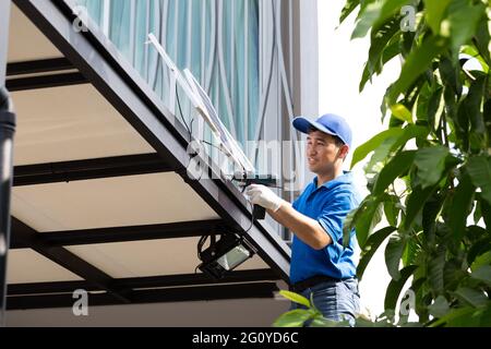 Asian workers technicians man installing solar photovoltaic panels for LED lamps on the roof of the house. Exterior solar cell system installation con Stock Photo