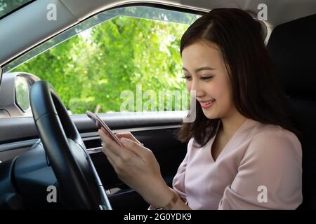 Asian woman using phone and sending a message behind the wheel, Female driving a car with using navigation or application on smartphone, Smart technol Stock Photo