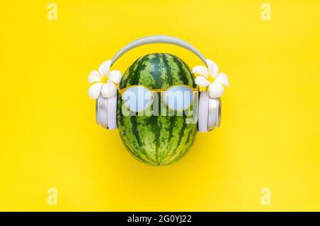 Watermelon wearing wireless headphone with white frangipani flowers on yellow background. Minimal summer concept. Stock Photo