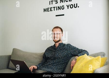 businessman sitting on sofa and using laptop. Confident male with laptop sitting on sofa in lobby. Stock Photo