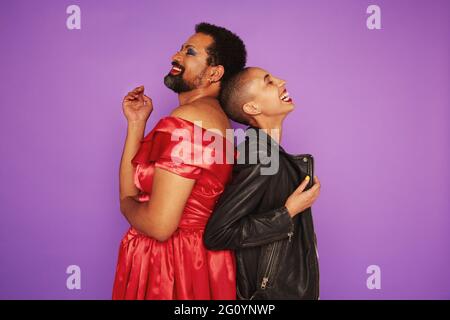 Man dressed as a woman and a woman dressed as a man smiling on purple background. Stock Photo