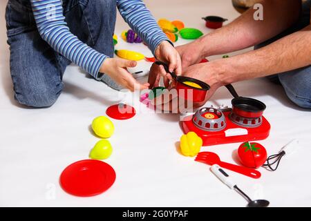 Dad and daughter play with sliced plastic vegetables and fruits with Velcro, cooks food on a toy stove in a bowl. Children's cooking, a girl learns to Stock Photo