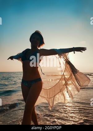 Young woman in white cover up dancing on the beach on  sunset Stock Photo