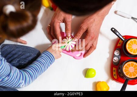 Dad and daughter play with sliced plastic vegetables and fruits with Velcro, cooks food on a toy stove in a bowl. Children's cooking, a girl learns to Stock Photo