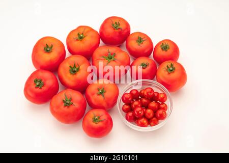 Closeup top view showing red cherry tomatoes in bowl  surrounded by big tomatoes arranged on white background . Stock Photo