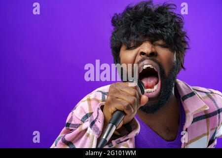 Young bearded african american man singing in microphone against purple background Stock Photo
