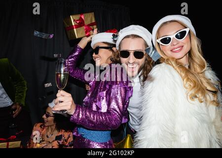 happy interracial friends in santa hats drinking champagne and celebrating new year on grey background Stock Photo