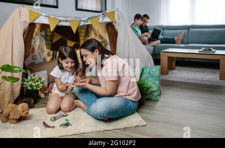 Mother and daughter playing while father and son use laptop Stock Photo