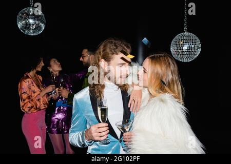 smiling couple hugging on party with multiracial friends on black background Stock Photo