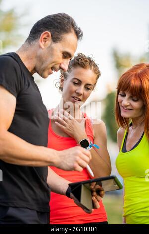 Male personal trainer holding a tablet and showing women what the workout will be. Stock Photo