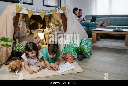 Children playing camping at home while their parents work with laptop Stock Photo