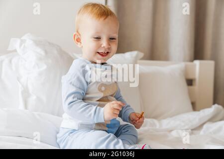 Happy blonde baby boy smiling while playing on bed at home Stock Photo