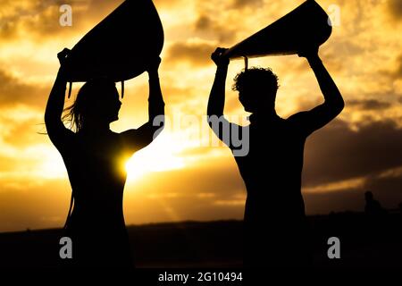 Silhouette of surfer people carrying their surfboards on sunset beach. Sport and friendships concept. Stock Photo