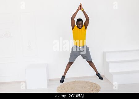 Athletic Afro American male jumping, warming up during sport workout at home. Energetic sporty man in yellow sportswear doing jumping exercise Stock Photo