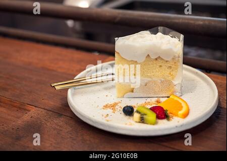 Coconut vanilla cake with whipped cream and berry fruits on plate in bakery shop Stock Photo