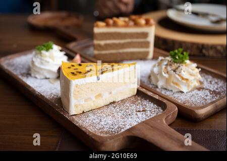 Passion fruit cake with vanilla layer, whipped cream and icing on wooden tray in the cafe Stock Photo