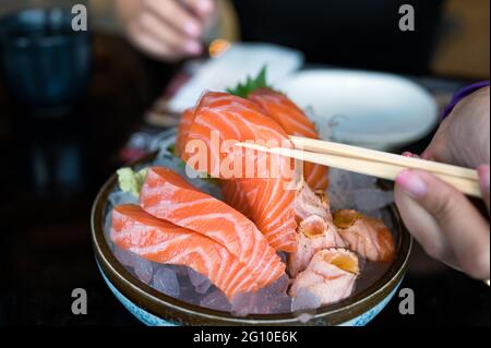 Hand with chopsticks holding sashimi sliced salmon on bowl in japanese restaurant Stock Photo