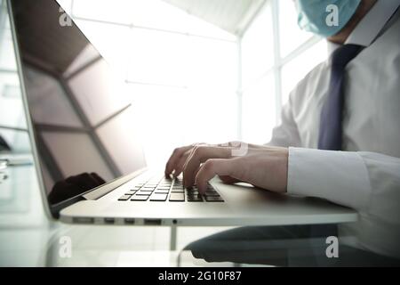 Concentrated young male professional wearing breath protective mask, working on computer Stock Photo
