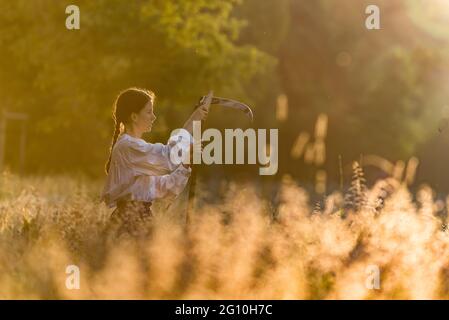 Prague, Czech Republic. 04th June, 2021. A woman sharpens the scythe during sunrise. Once per year flower meadow in Stromovka park, one of the biggest park in the Prague, is manually mown in order to save folk tradition. Credit: SOPA Images Limited/Alamy Live News Stock Photo