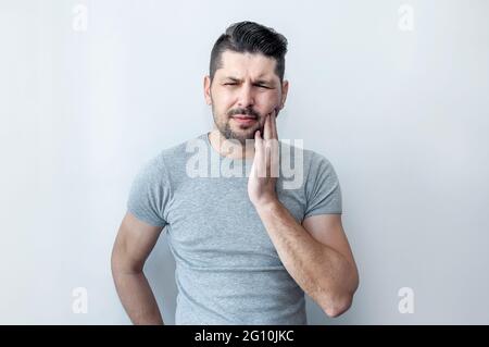 Toothache concept. Frustrated young man touching his cheek suffering terrible strong teeth pain. Stock Photo