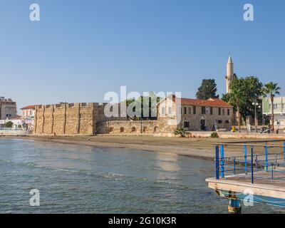 View from the pier over the ancient Larnaca fortress, the tower of Djami Kebir Mosque, and beach with volcanic sand on a sunny day in Cyprus. Stock Photo