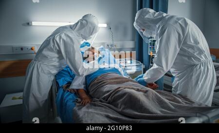 Hospital Coronavirus Emergency Department Ward: Team of Doctors wearing Coveralls, Face Masks Take Care of a Senior Patient Lying in Bed, Put Oxygen Stock Photo