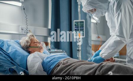 Hospital Coronavirus Emergency Department Ward: Doctors, Paramedics wearing Coveralls, Face Masks Save Life of a Senior Female Patient Lying in Bed Stock Photo