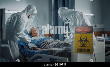Hospital Coronavirus Emergency Department Ward: Doctors wearing Coveralls, Face Masks Save Life of a Senior Patient Lying in Bed, Put Oxygen Mask and Stock Photo