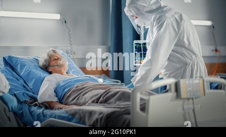 Hospital Coronavirus Emergency Department Ward: Team of Doctors wearing Coveralls, Face Masks Take Care of a Senior Patient Lying in Bed, Put Oxygen Stock Photo