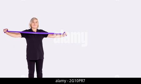 Everyday health for aged people. Sporty senior woman in black sportswear holding rubber resistance band while going to exercise at home. Workout, body Stock Photo