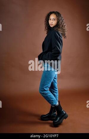 Young attractive woman poses in studio, showing off urban cloth, sloppy elegance. Studio photo. Stock Photo