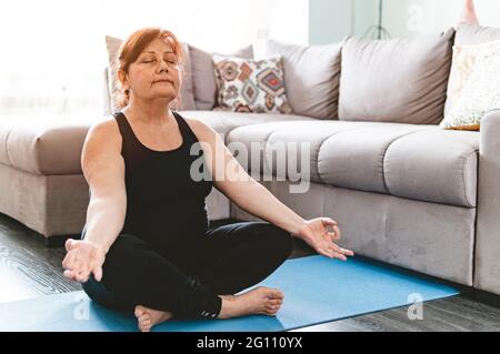 Middle aged woman in yoga position keeps fit in her home - Elderly person has fun doing sports - mental and physical well-being concept - warm filter Stock Photo