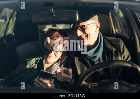 Retired couple on vacation consults directions on smart phone gps - active seniors traveling enjoy free time and retirement - focus on man hand Stock Photo