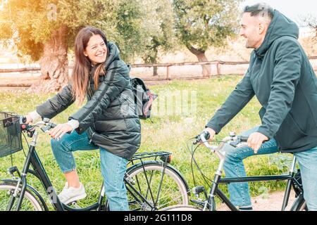 Young engaged couple take a walk in the countryside with bicycles - friends have fun riding the bike - warm flare on the left Stock Photo