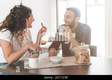 Engaged couple having breakfast together in their new home - young couple talking while eating and drinking in the kitchen - warming the filter on bac Stock Photo