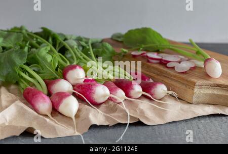 On the wooden surface of the table is a bunch of young radishes with green leaves. Stock Photo