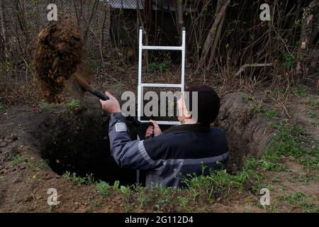 Man digs a huge pit. In his hands he holds a shovel, next to a man is a ladder. Stock Photo