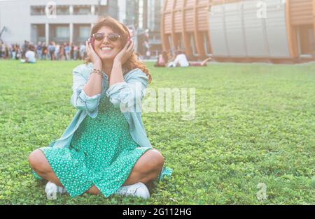 Young woman listens to music in the city park with wireless headphones - wellness and freedom concept Stock Photo