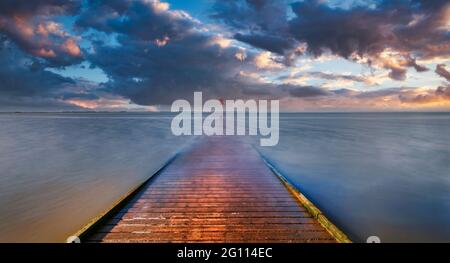 The wooden jetty at Lytham in Lancashire, UK, stretches out over the sandy beach and into the Irish sea as the sun sets creating a dramatic sky Stock Photo