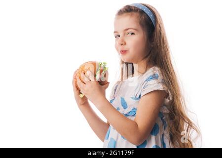 Little girl eating big burger. Kid looking at healthy big sandwich, studio isolated on white background. Stock Photo