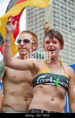 Couple celebrating at pride parade in toronto, man and woman smiling and sloganeering with a bright flag waving in the background