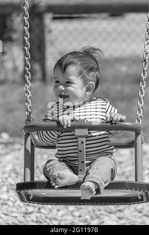 Vertical grayscale closeup shot of a male child on a swing Stock Photo