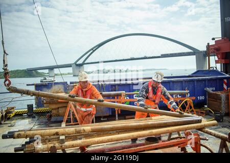 Fehmarn, Germany. 04th June, 2021. Premslaw Niecieki (l-r) and drilling technician Sergej Reinhardt dismantle the rods of a borehole on a drilling rig during test drilling in the Fehmarn Sound. The drilling is being used to plan the construction of the Fehmarnsund Tunnel between the Schleswig-Holstein mainland and the island of Fehmarn. The Fehmarnsund Bridge can be seen in the background. Credit: Gregor Fischer/dpa/Alamy Live News Stock Photo