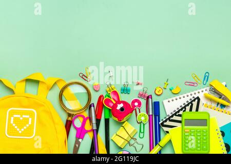 Frame from of office supplies Paper clips, scissors, pens, felt-tip pens, sharpener, backpack, calculator, stapler isolated on green background Flat l Stock Photo